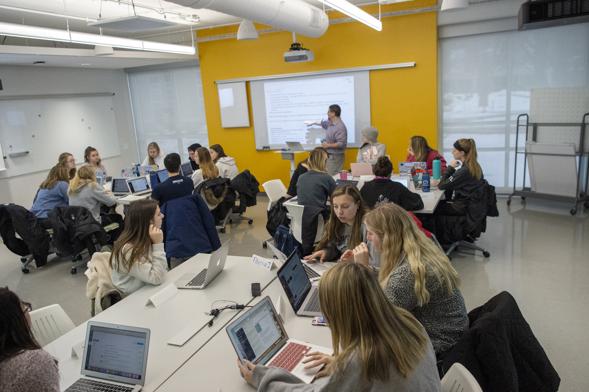 Classroom of students with laptops and faculty member in front of a projection screen