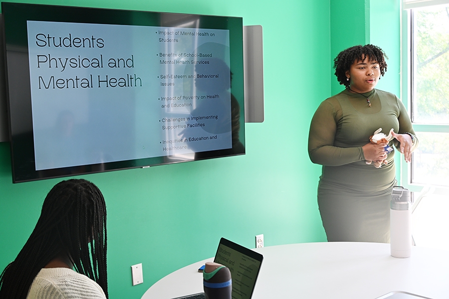 A SCOPE student gives a presentation in a room with green walls.